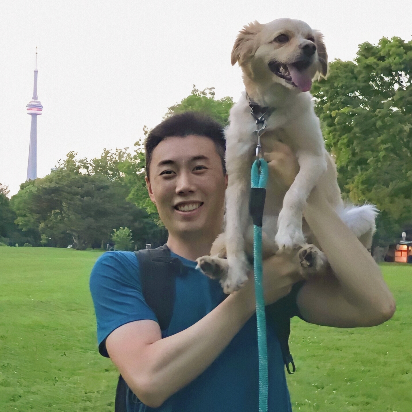 Yi Liu holds his dog up on his shoulder in a park