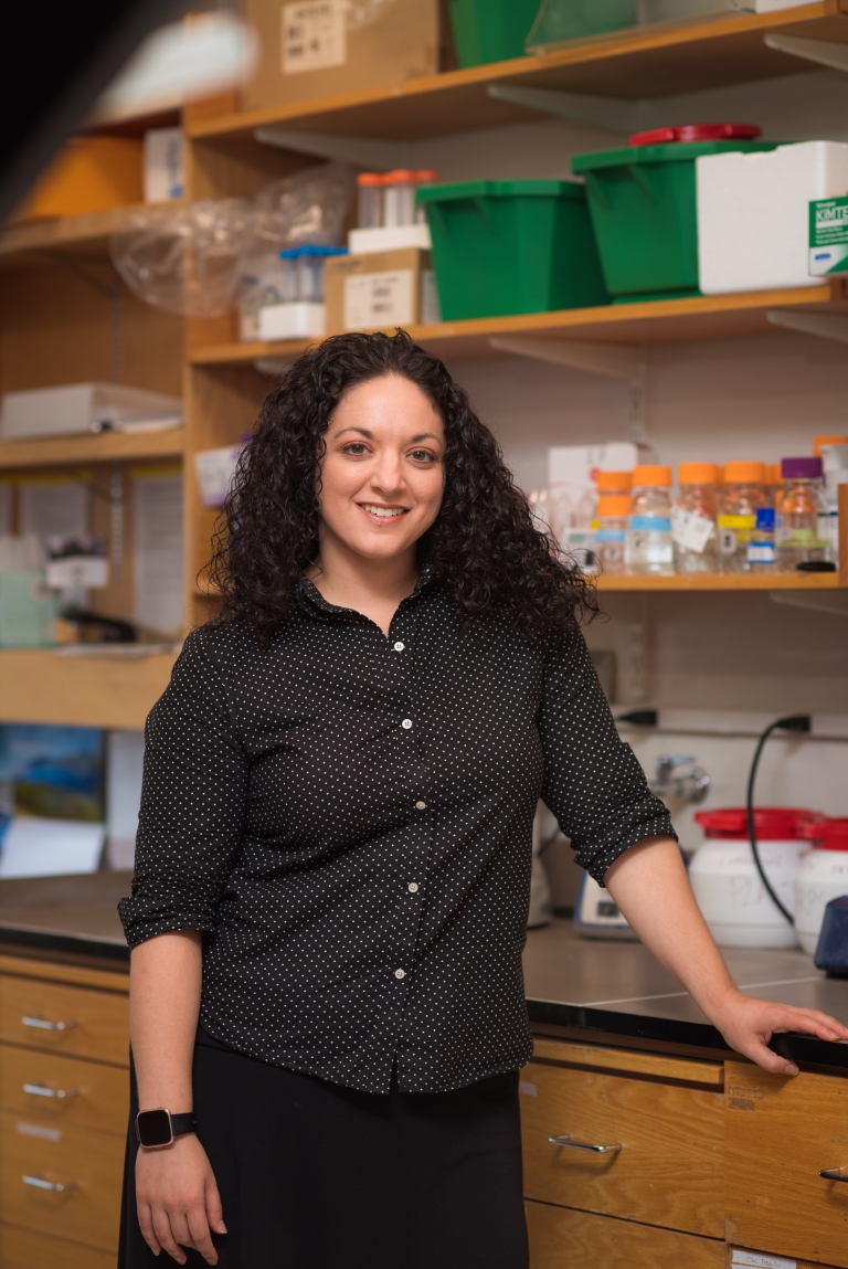 Olivia Corradin stands smiling at a lab bench.