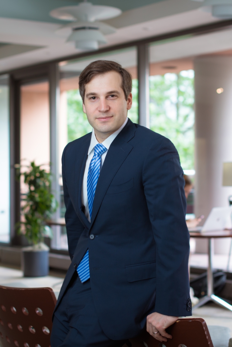 A man in a suit leans on a desk