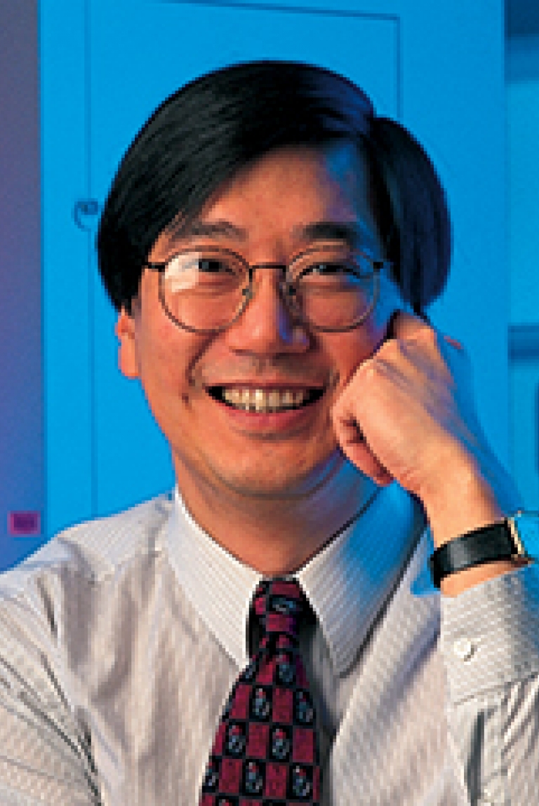 A man leans his face on his hands in front of a blue background.