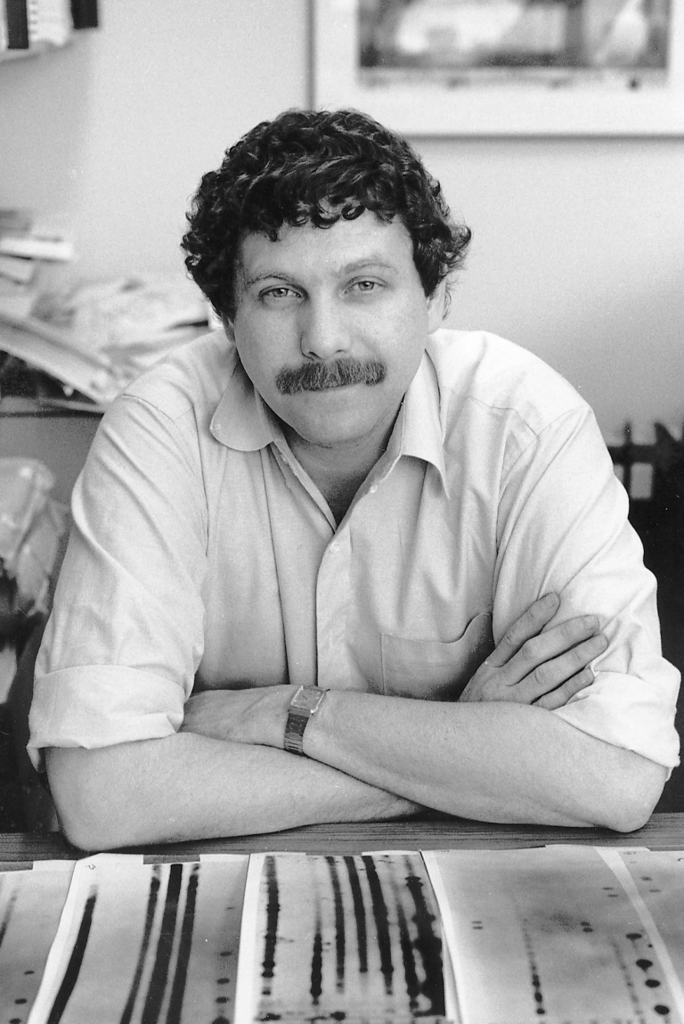 A man with a mustache leans on a table.