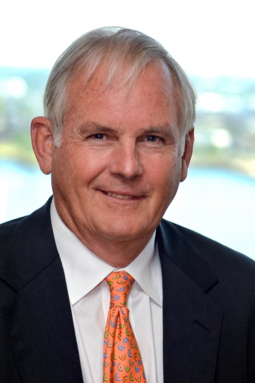 A man in an orange tie smiles in front of a green and blue background.