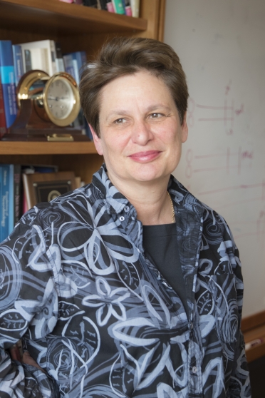 A woman in a flowered shirt stands in front of a bookshelf