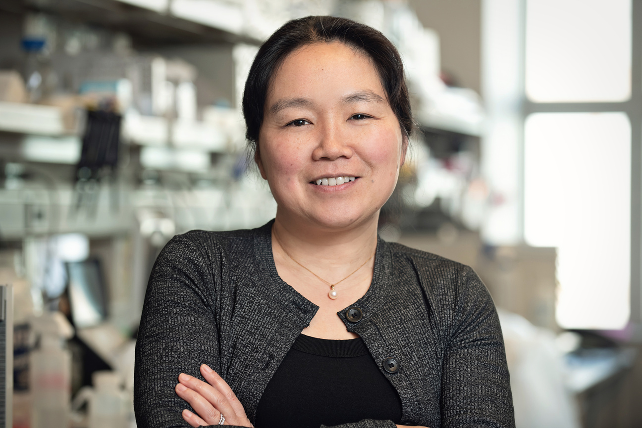 A woman in a grey cardigan stands smiling in a lab.