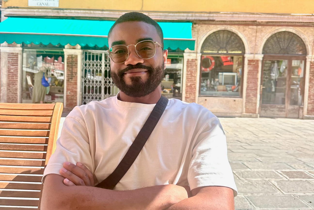 Christopher Reid sits with arms crossed, wearing tinted glasses in a sunny outdoor square