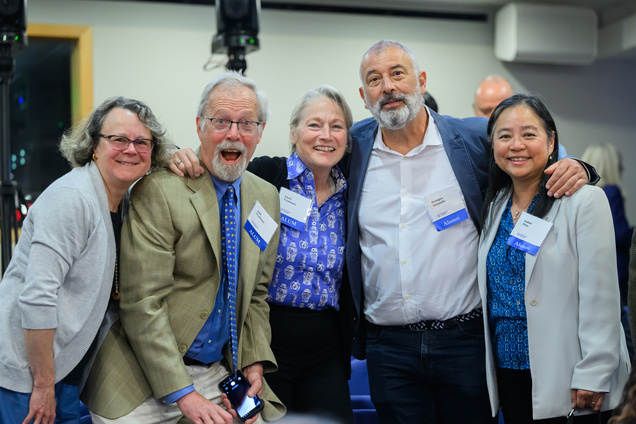 Five smiling people, four with visible alumni tags, standing together for a photo op