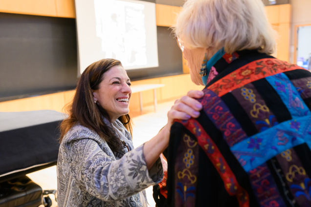 A woman smiling, with her hand on another woman's shoulder, and the front of the auditorim behind them