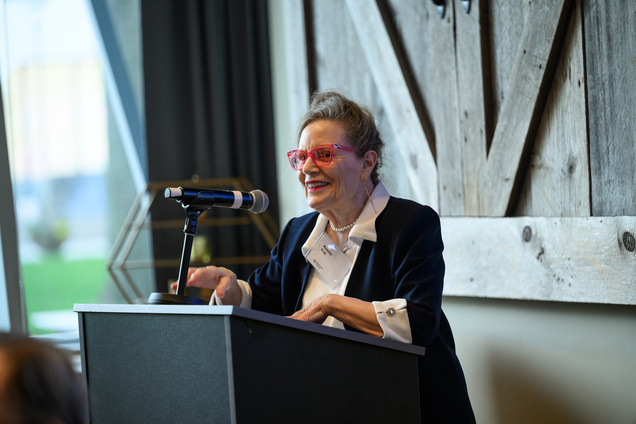 Rosalie Fink speaking in front of a podium with arge wooden doors behind