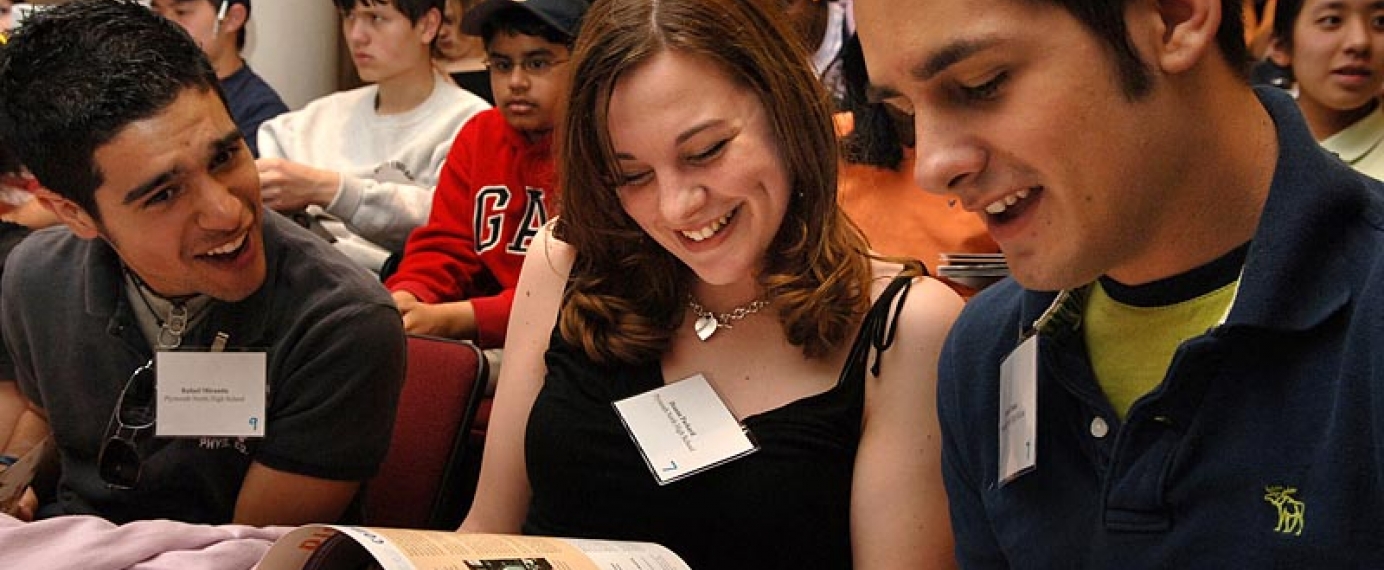 High school students look at handouts during a lecture, laughing.