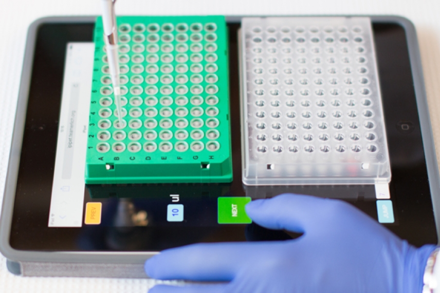 Image of iPipet - a gloved purple hand holds an iPad, and a pipette hovers over well plates on top of the screen